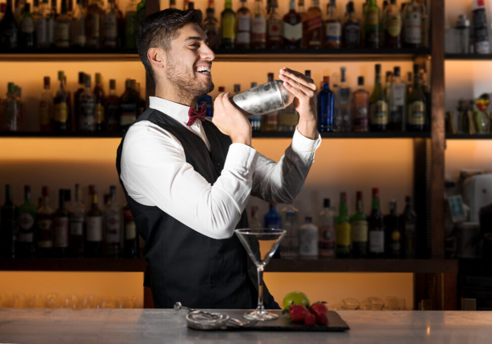 Cool professional bartender making a cocktail, shaking a cocktail shaker. Authentic barman making alcohol beverages in modern bar. High quality photography.